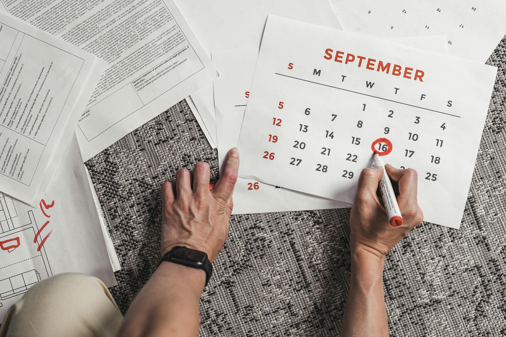 Pricing Hands holding a calendar with September dates encircled, surrounded by documents on a carpet.