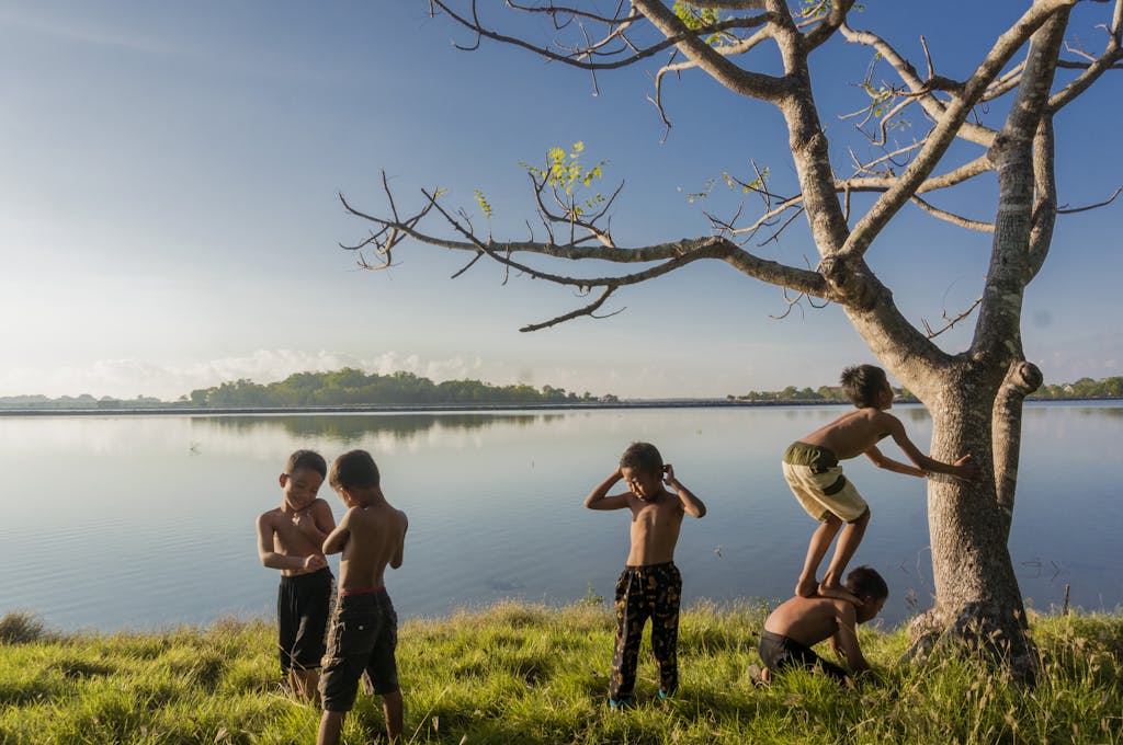 Home Five kids enjoy a playful day by the lake, climbing trees and bonding under clear skies.